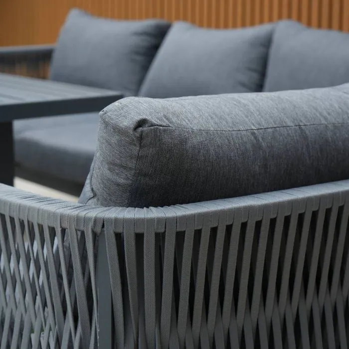 Aurora lounge garden furniture set featuring a modern grey rope design with comfortable cushions and fire pit table. Elegantly arranged in a garden setting with sleek cladding in the background